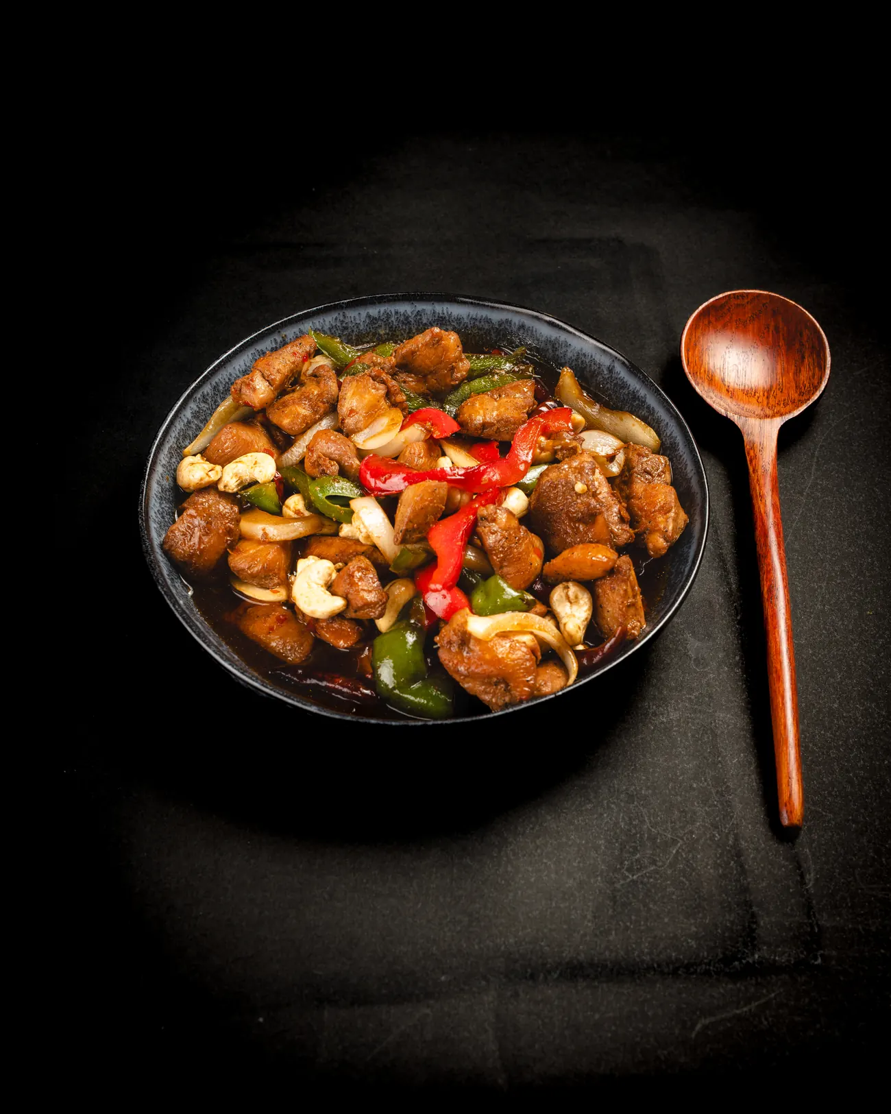 Bowl de pollo salteado con cuchara de madera sobre fondo negro