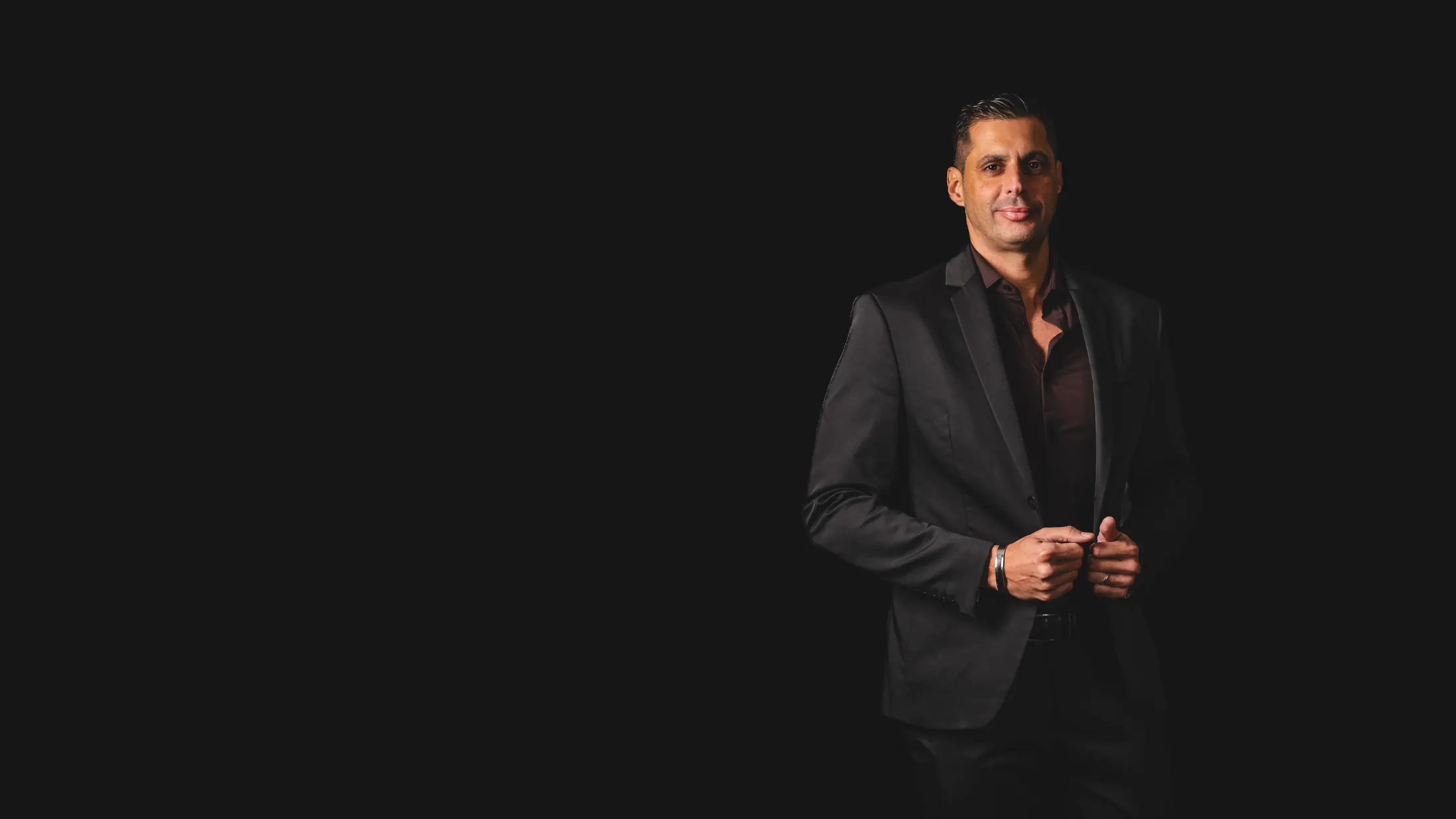 Retrato corporativo de un empresario con traje oscuro sobre fondo negro