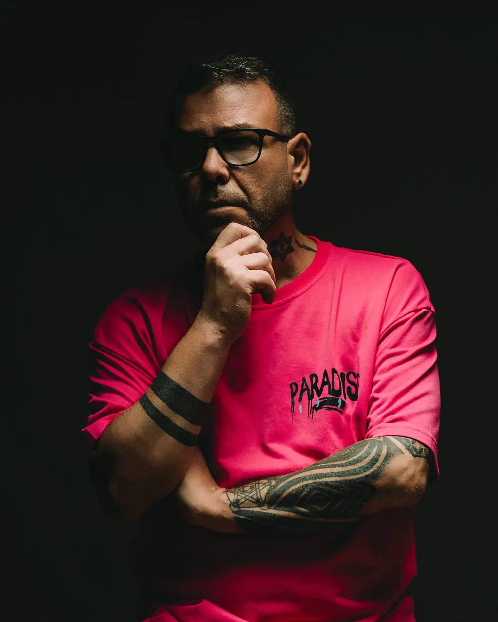 Retrato de estudio de Jose Richarte con camiseta rosa y gafas, fondo oscuro