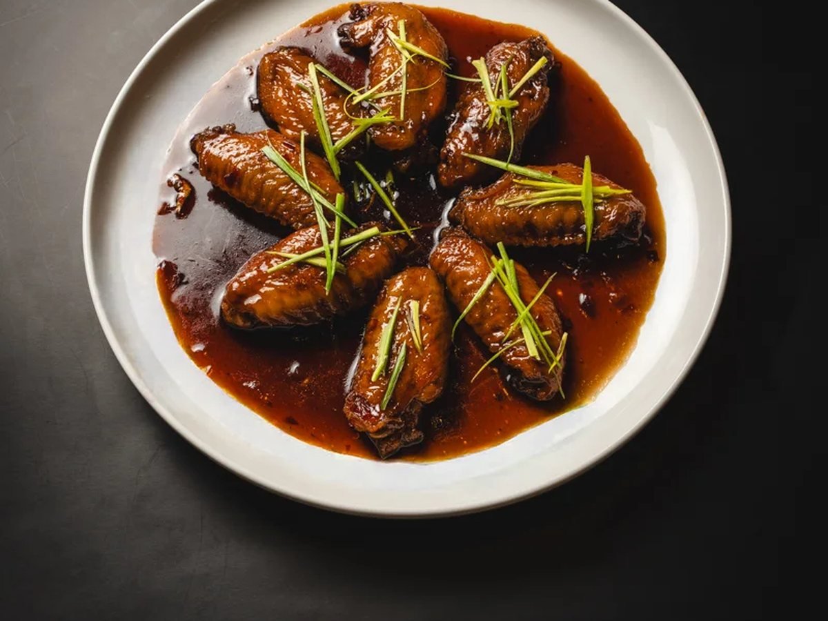 Alitas glaseadas en plato blanco sobre fondo negro, fotos con estilo coherente para la carta
