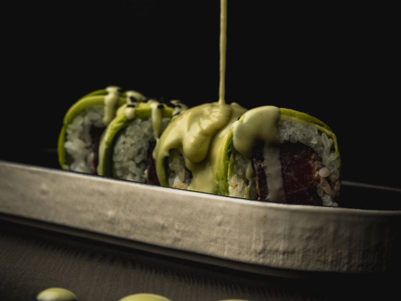 Rollo de sushi con salsa de aguacate centrado sobre fondo oscuro, foto para carta de delivery