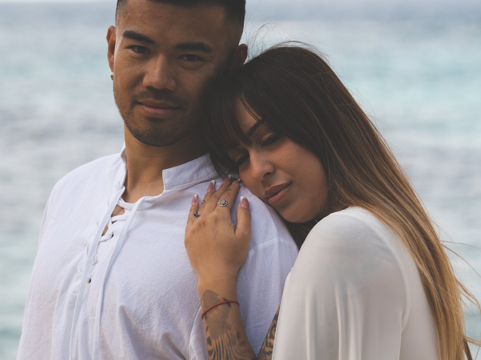 Pareja con ropa blanca de lino abrazada junto al mar en Mallorca