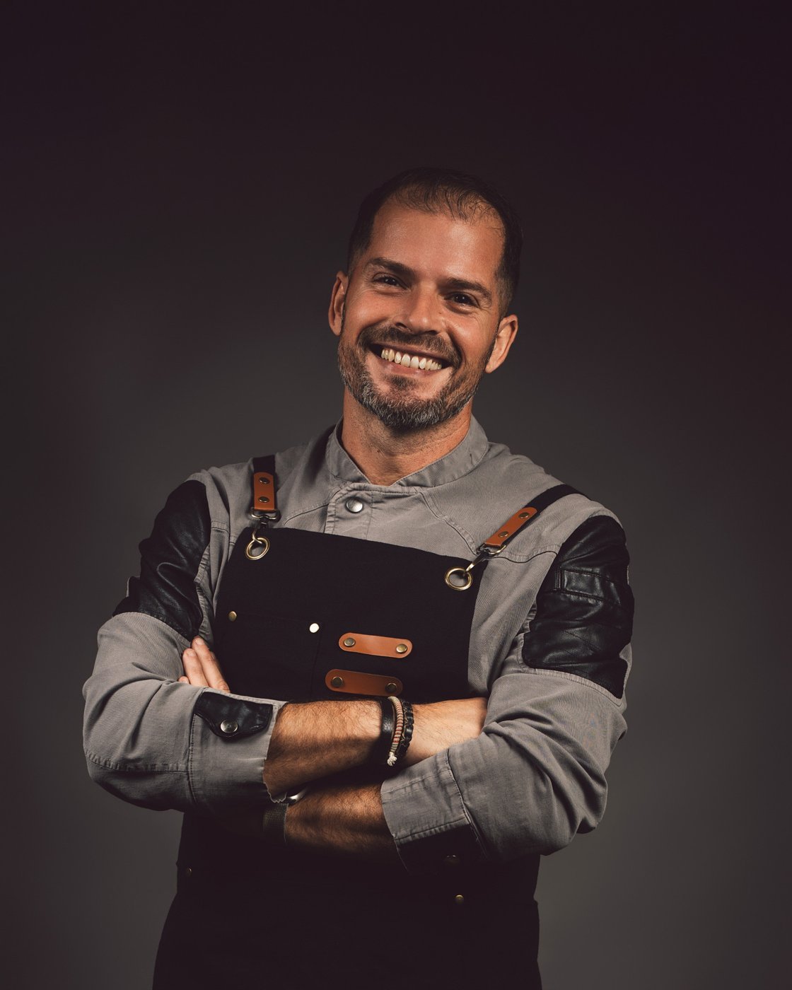 Chef sonriente con delantal de cuero y brazos cruzados, retrato de chef en estudio en Mallorca