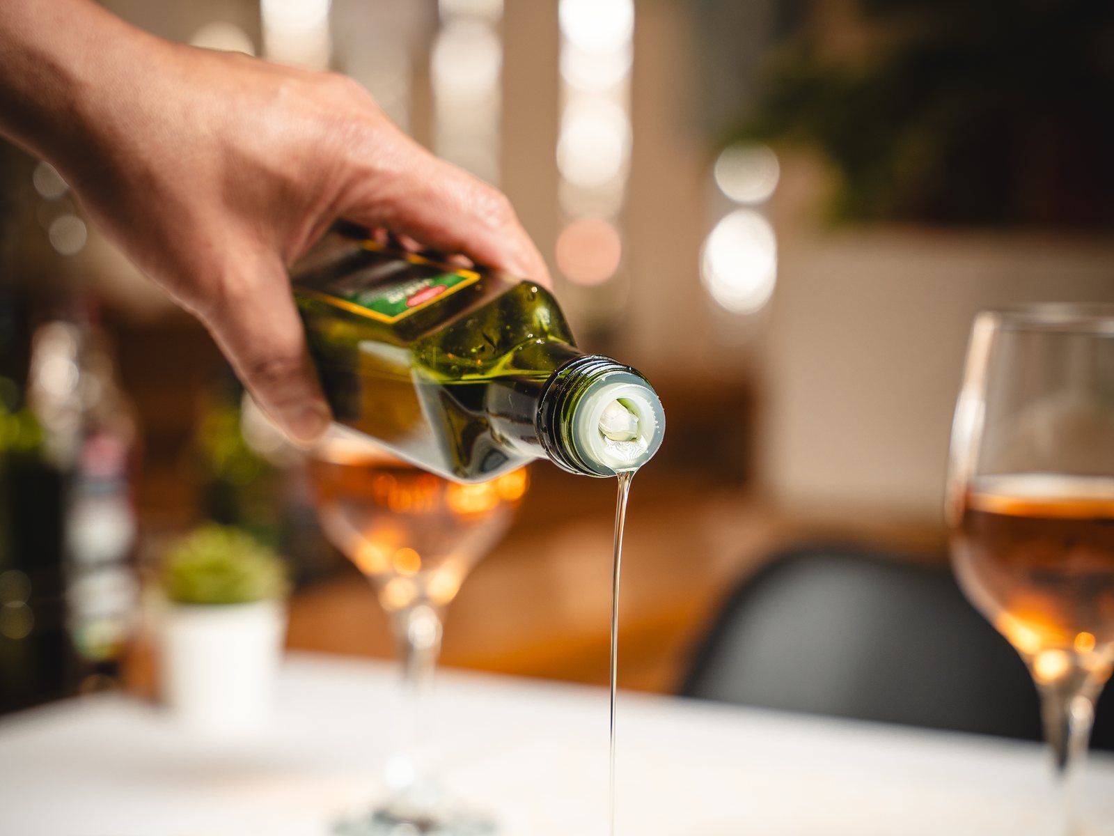 Mano sirviendo aceite de oliva sobre un plato en una mesa montada con copas de vino, foto de sala de restaurante